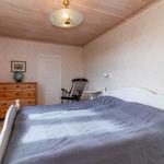 Schlafzimmer mit weißem Bett, Holzdecke und Schrank. Wanduhr und Stuhl sind sichtbar.