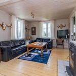 Wohnzimmer mit Ledersofa, Holztisch und Kaminofen. An den Wänden hängen Geweihdekorationen.