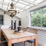 Essbereich mit Holztisch, Stühlen und Kronleuchter. Große Fenster zeigen grüne Bäume.