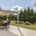 Terrasse mit Pavillon, Tisch und Stühlen. Grünfläche mit Bäumen und Felsen im Hintergrund.