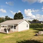 Ein Ferienhaus mit Terrasse, Garten und Blick auf Bäume unter blauem Himmel.