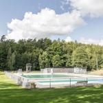 Ein Schwimmbad mit Sprungturm und Umzäunung im Grünen.