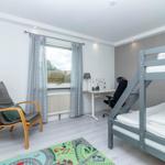 Zimmer mit Doppelstockbett, Schreibtisch und Sitzgelegenheit. Fenster mit Gardinen.