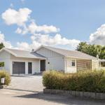 Moderne Villa mit Garage, Terrasse und grüner Umgebung unter blauem Himmel.