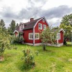 Rotes Holzhaus mit grünem Garten und Bäumen im Hintergrund.