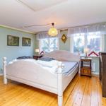 Schlafzimmer mit Bett, Nachttischen und Fenster. Holzboden und hellblaue Wände.