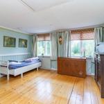 Ein Schlafzimmer mit Holzboden, weißem Bett und Holzschränken. Fenster mit Vorhängen.