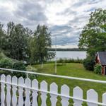 Weitläufiger Garten mit Blick auf See und rote Scheune. Weiße Brüstung im Vordergrund.