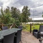Terrasse mit Tisch, Stühlen und Grill, Blick auf See und Bäume.