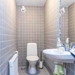 Badezimmer mit Toilette, Waschbecken und Spiegel. Wände sind mit Fliesen verkleidet.