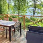 Holzterrasse mit Tisch, Stühlen und Liege, Blick auf See und Bäume.