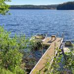 Holzsteg mit zwei Booten am Ufer eines Sees mit Wald im Hintergrund.