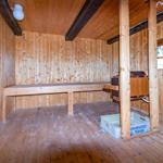 Holzsauna mit Bank, Ofen und Fenstern. Boden und Wände aus Holz.