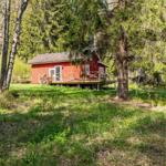 Rotes Holzhaus mit Veranda im Wald. Grasland und Bäume umgeben die Unterkunft.
