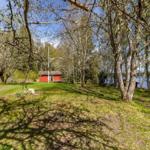 Rotes Haus mit Terrasse im Wald, Blick auf See und grünes Gras.