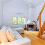 Wohnraum mit Sofa, Kamin und Holztreppe. Fenster mit Blick auf Grün.