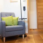 Ein grauer Sessel mit zwei grünen Kissen steht auf Holzfußboden.