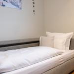 Ein Bett mit weißen Kissen und Bettwäsche. An der Wand hängt ein Bergbild.