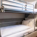 Doppelstockbett mit Matratzen und Kissen. Metallgestell und graue Polsterung.