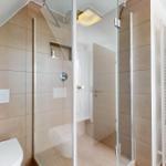 Bad mit Dusche, Toilette und Heizkörper an der Wand.