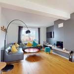 Wohnzimmer mit grauem Sofa, rotem Tisch und Fernseher an grauer Wand.