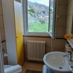 Badezimmer mit Waschbecken, Toilette und Fensterblick auf grüne Hügel.