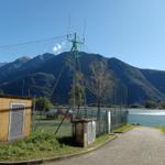 Pfad entlang des Sees mit Sportplatz und Bergen im Hintergrund.