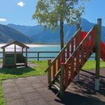 Kinderbereich mit Rutsche und Hütchen am See mit Bergen im Hintergrund.