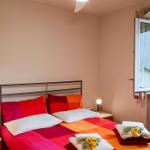 Schlafzimmer mit Bett, Nachttischen und Fenster. Bett mit bunten Kissen und Handtüchern.