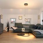 Wohnzimmer mit grünem Sofa, Glas-Tisch und Fernseher auf grauem Schrank.