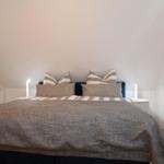 Schlafzimmer mit Bett, Nachttischen und Kleiderschrank. Wandfarbe weiß, Holzboden.