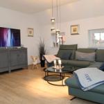 Wohnzimmer mit grünem Sofa, Fernseher und Glas-Tisch.