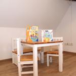 Kindertisch mit Stühlen und zwei Büchern auf Holzfußboden.