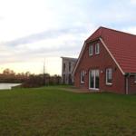 Rotes Ziegeldach, großer Garten und Wasser im Hintergrund. Modernes Haus mit Glasfront.