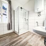 Badezimmer mit Dusche, Waschbecken und Fenster mit Blick auf Gebäude.