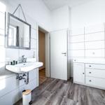 Badezimmer mit Waschbecken, Spiegel und Schrank. Holzdielenboden und weiße Fliesen.