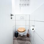 WC mit Holzdeckel, Toilettenpapierhalter und Fenster mit Herzvorhang