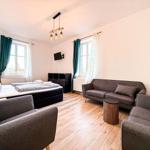 Zimmer mit Bett, Sofa, Stühlen und TV. Holzboden und Fenster mit Vorhängen.