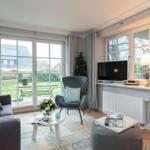 Wohnzimmer mit Sofa, Sessel und Fernseher. Durchgangstür zum Garten.