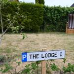 Schild mit Parkplatz für The Lodge 1, Rasenfläche mit Stuhl und Hecke im Hintergrund.
