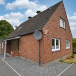 Rotes Backsteingebäude mit Dach und Fenstern. Vorhof mit Kies und Pflanzen.