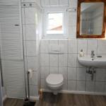 Badezimmer mit Dusche, Toilette und Waschbecken. Fliesenwand und Holzboden.