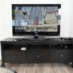 Flachbildfernseher auf schwarzer TV-Einheit mit Fernbedienungen und Receiver.