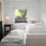 Zimmer mit zwei Betten, Schrank, Nachttisch und Fenster mit Blick auf Grün.