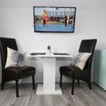 Esstisch mit zwei Stühlen, Fernseher und Kühlschrank in einem Raum.