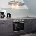 Küche mit Dunstabzugshaube, Herd, Spüle und Kaffeemaschine.