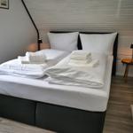 Schlafzimmer mit Doppelbett, weißen Laken und Handtüchern. Holzboden und schlichte Einrichtung.