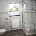 Badezimmer mit Dusche, Toilette und Fenster mit Blick auf Grün.