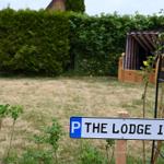 Schild mit Parkplatz für The Lodge 11. Hintergrund: Rasen, Hecke und Pavillon.