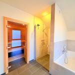 Dusche, Badewanne und Sauna in einem Raum mit Holz- und Fliesenverkleidung.